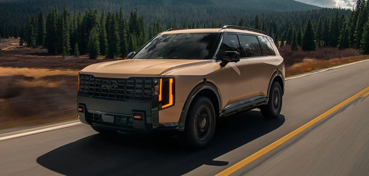Tan 2027 Kia Telluride driving on a mountain highway