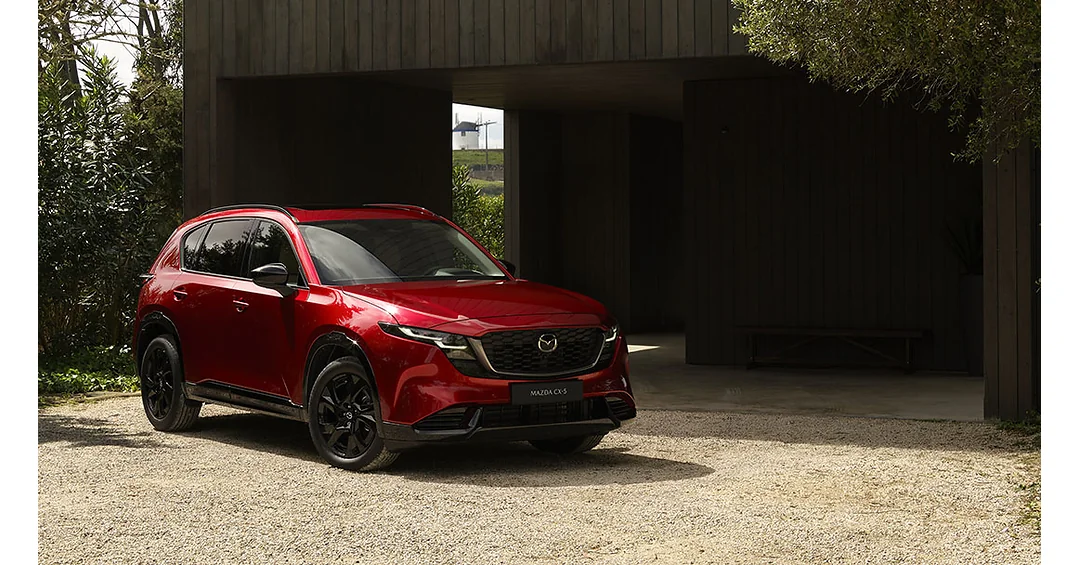 Red Mazda CX-5 parked on gravel in front of a dark wooden building
