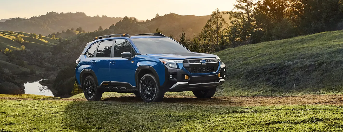 Blue 2027 Subaru Forester Wilderness parked on a grassy hillside